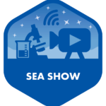 A hexagonal badge in shades of blue, titled "SEA SHOW." It features icons including a microscope, a beaker, a video camera, and a WiFi signal, all set against a backdrop of stars. This design suggests a focus on scientific discovery and media or communication in a marine setting.